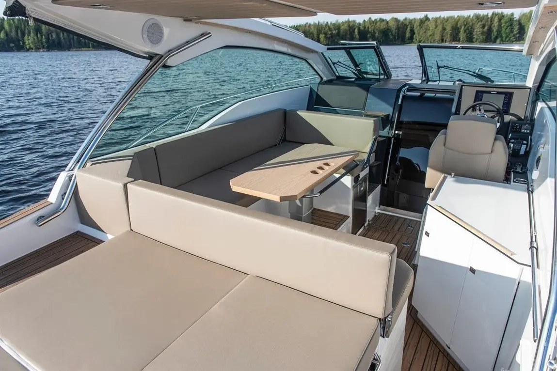 Luxury boat interior features a spacious seating area, wooden table, helm console, and views of calm water and forest.